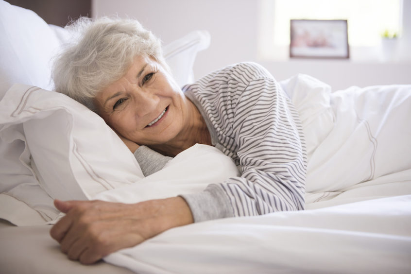 Older woman with short hair lying in bed with a smile on her face after having a restful night of sleep.