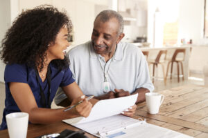 Happy female healthcare worker sitting at table smiling with a senior man during a home health visit