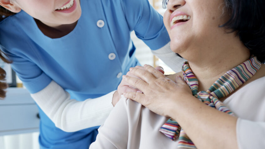 Young home nurse laughing, holding hand of older woman.