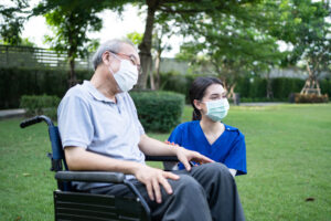 Female nurse in mask with man in wheelchair and mask outside.