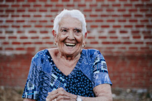 Older woman in blue shirt laughing on brick background.